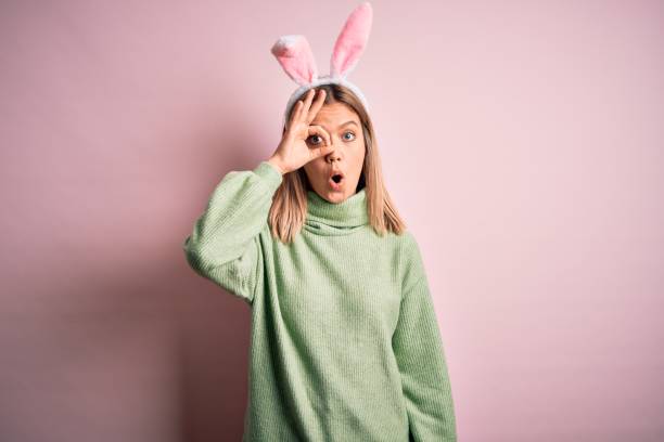 istock Young beautiful woman wearing easter rabbit ears standing over isolated pink background doing ok gesture shocked with surprised face, eye looking through fingers. Unbelieving expression. 1212376179