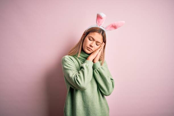 istock Young beautiful woman wearing easter rabbit ears standing over isolated pink background sleeping tired dreaming and posing with hands together while smiling with closed eyes. 1212376213
