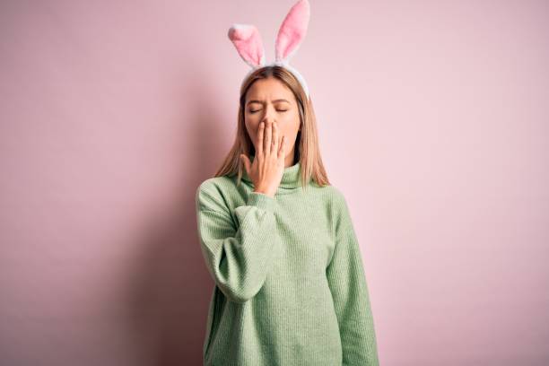istock Young beautiful woman wearing easter rabbit ears standing over isolated pink background bored yawning tired covering mouth with hand. Restless and sleepiness. 1212376216