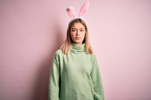 istock Young beautiful woman wearing easter rabbit ears standing over isolated pink background Relaxed with serious expression on face. Simple and natural looking at the camera. 1212376228
