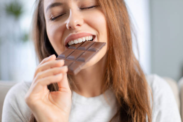 Woman biting a chocolate bar Cheerful young woman eating chocolate at home chocolate stock pictures, royalty-free photos & images
