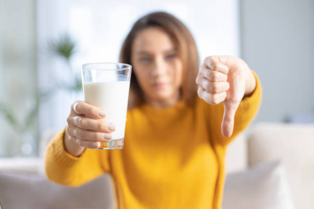 Young woman with glass of milk, negative sign showing dislike with thumbs down Young woman with glass of milk, negative sign showing dislike with thumbs down. Lactose intolerance concept lactose fermentation stock pictures, royalty-free photos & images