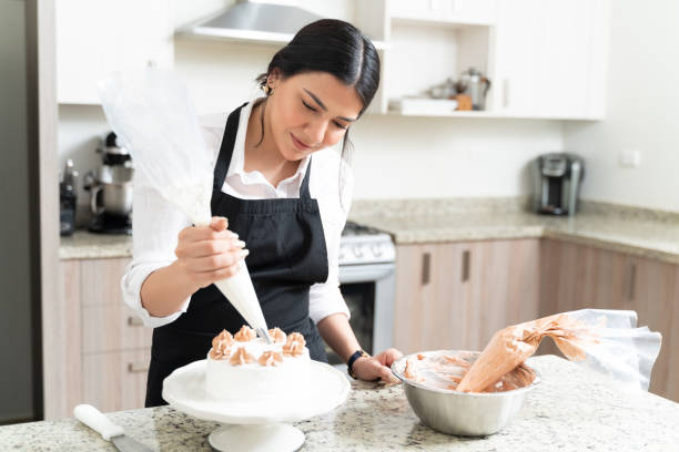 Beautiful Female Pastry Chef Preparing Cake At Home Gorgeous young baker decorating cake with pastry bag on counter in kitchen decorating a cake photos stock pictures, royalty-free photos & images