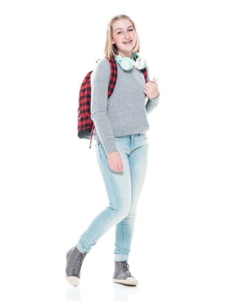 istock Generation z female student standing in front of white background wearing backpack and holding textbook and using headphones 1212391072