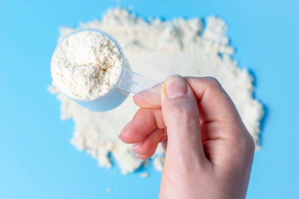 istock Female hand holds measuring spoon with protein on a blue background top view. 1212393053