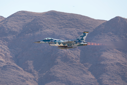 F-16 Fighting Falcon in the Aggressor color scheme  against the Nevada hills, with missiles on the wing, afterburner on and  the jet stream visible behind the aircraft
