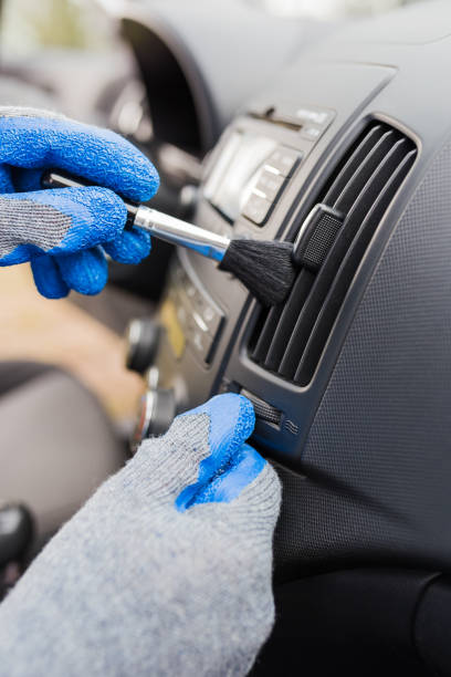 istock Man hands wearing protective gloves using cleaning brush and removing dust from car air conditioning vent grill. Car detailing or valeting concept. 1212395776