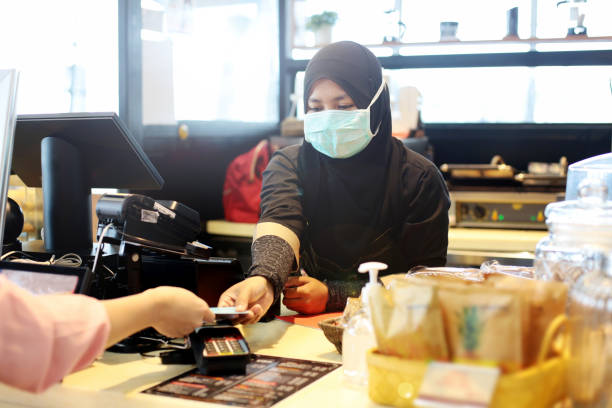South East Asia: At The Airport A Muslim female adult is holding credit card for processing contactless payment at airport cafe cashier counter in Malaysia. klia airport stock pictures, royalty-free photos & images