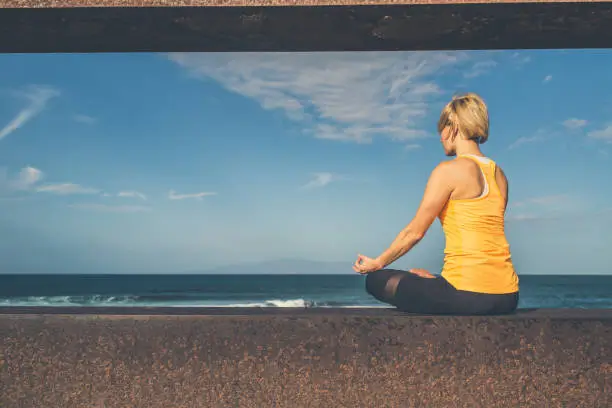 Woman meditating in yoga pose, ocean view, beach and wooden sidewalk. Motivation and inspirational summer sea landscape. Healthy lifestyle outdoors in nature concept.