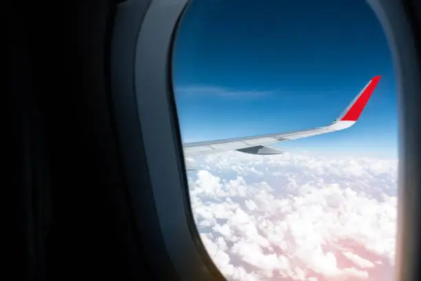 Photo of Airline low-cost flight  wing in the morning with beautiful white cloudy sunrise. Airplane wing outside of window shades.