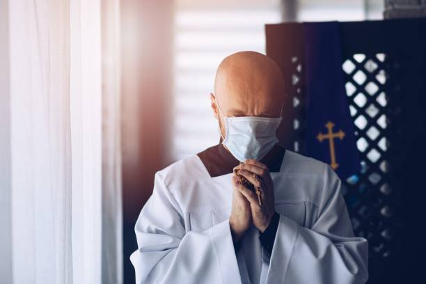 Man priest in medical mask praying with cross and rosary. Man priest in medical mask praying with cross and rosary. Church during corona virus epidemic. clergy stock pictures, royalty-free photos & images