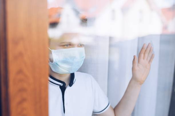 istock Sad child boy in medical mask looking through the window. Quarantine 1212404893