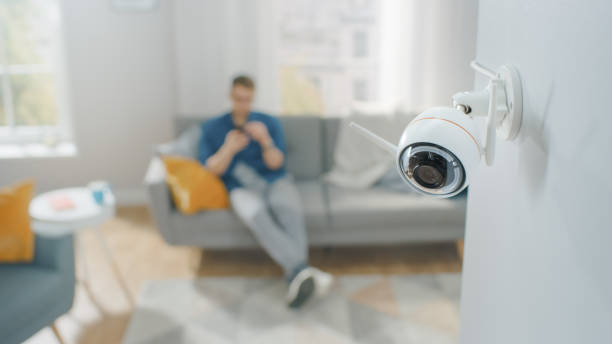 närbild objekt skott av en modern wi-fi övervakningskamera med två antenner på en vit vägg i en mysig lägenhet. man sitter på en soffa i bakgrunden. - security home bildbanksfoton och bilder