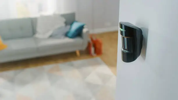 Photo of Close Up Object Shot of a Modern Movement Detector Unit on a White Wall in a Cozy Apartment in the Background.