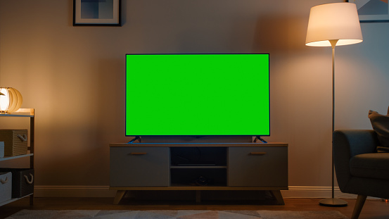Toma de un televisor con pantalla verde horizontal Mock Up. Acogedor salón nocturno con una silla y lámparas encendidas en casa. photo