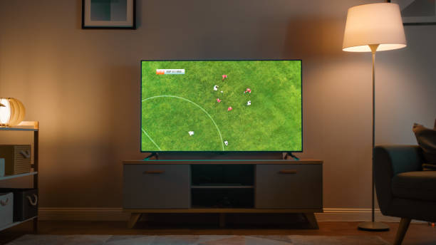 Shot of a TV with Soccer Match. Cozy Evening Living Room with a Chair and Lamps Turned On at Home. Shot of a TV with Soccer Match. Cozy Evening Living Room with a Chair and Lamps Turned On at Home. tv game stock pictures, royalty-free photos & images