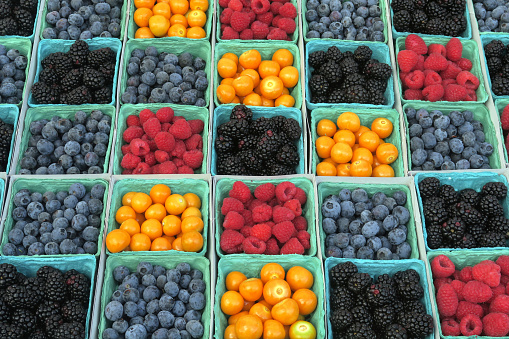 containers full of berries and little yellow tomatoes on display for sale at a farmer's market