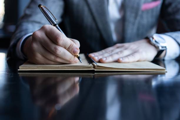 istock Man hand with pen writing on notebook on table. Man working at coffee shop. 1212412530