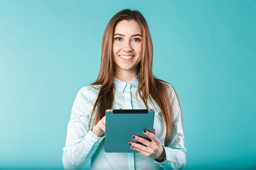 She always connected. Woman using digital tablet computer PC happy isolated on turquoise background. Portrait young caucasian woman worker, teacher, mentoring in shirt office style with tablet in hand