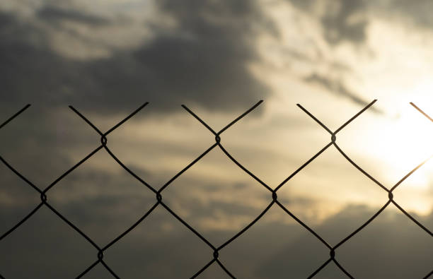 istock Restricted area concept. A metal mesh fence enclosing a restricted area (quarantine, prison, production area) 1212416825