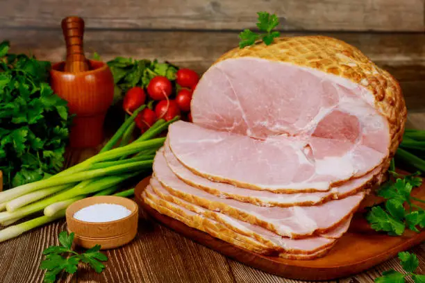 Smoked boneless ham with vegetables and salt on wooden Christmas table.
