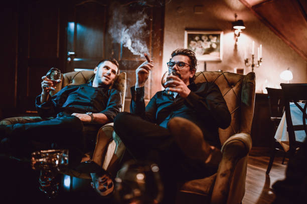 Mafia Family Father And Son Enjoying Good Cognac With Cigars And Conversation Mafia Family Father And Son Enjoying Good Cognac With Cigars And Conversation organized crime photos stock pictures, royalty-free photos & images