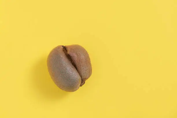 Ugly misshapen fruit kiwi on yellow background. Top view with copy space