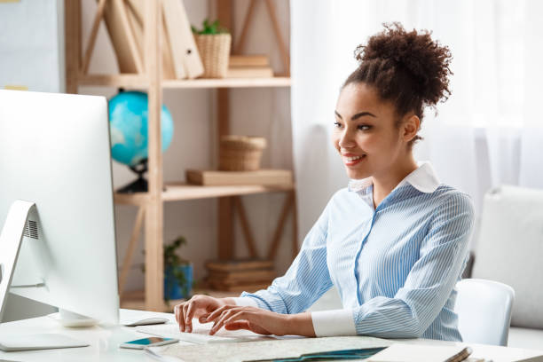 istock Tour agent sitting at table in office typing information on computer cheerful 1212427585