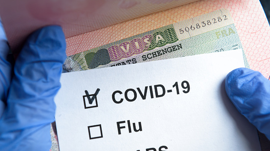 COVID-19 coronavirus pandemic and travel concept, positive mark COVID-19 and Schengen Visa stamp. Passport control of tourists with coronavirus check. Novel corona virus outbreak, epidemic in Europe.