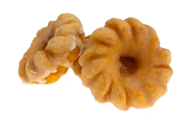 Side view of three glazed bite size crullers on a white background.