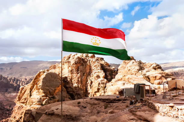 flag of tajikistan is flying in the wind against a cloudy sky in mountains. - tajik flag imagens e fotografias de stock