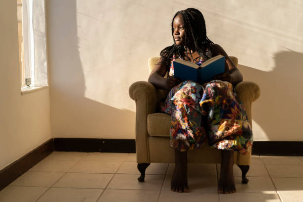 伝統的な服を着たアフリカ人女性が自宅に座って読書をする - braids african descent women pensive ストックフォトと画像