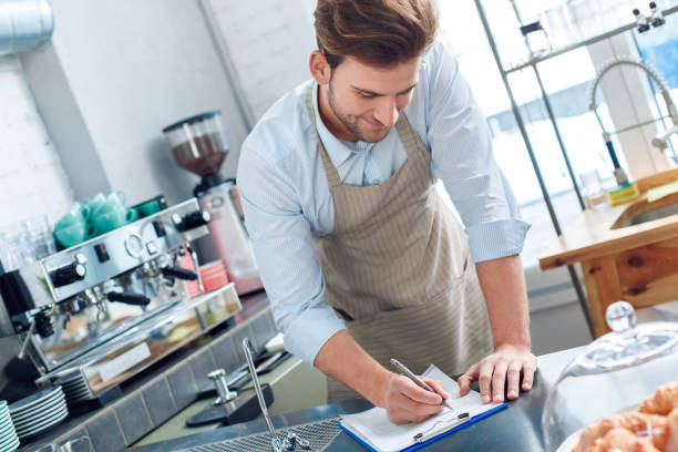 istock Young adult barista working in cafeteria, making notes 1212441172
