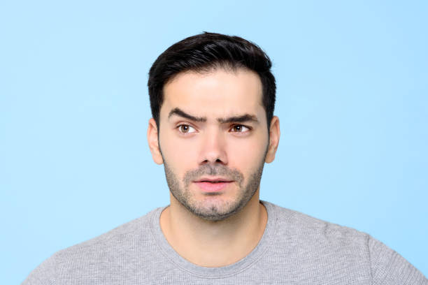 istock Thoughtful curious young man face with eyebrow raised isolated on light blue backgound 1212441245