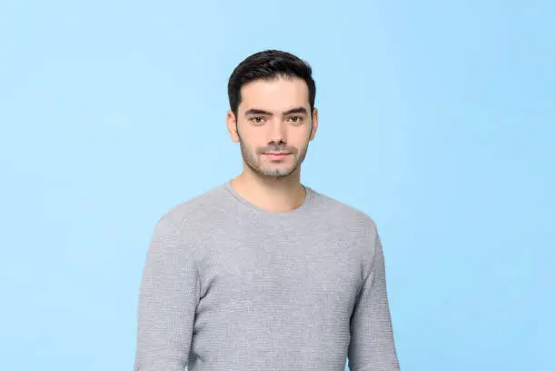 Waist up portrait of young handsome European man in plain gray t-shirt isolated in light blue bakground