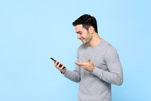 Smiling happy young man using smartphone isolated on light blue studio background