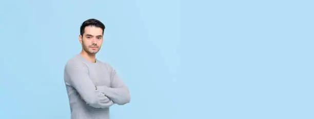 Confident handsome man in casual gray t-shirt doing arm crossed gesture isolated on light blue banner background with copy space