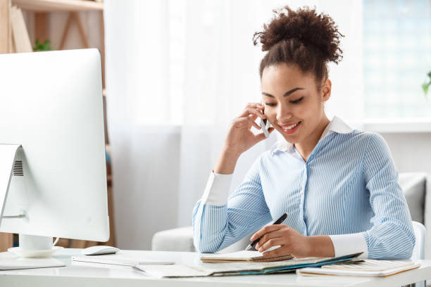 istock Tour agent sitting at table in office talking on smartphone with client taking notes joyful 1212441330