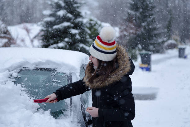 młoda atrakcyjna brunetka kobieta odśnieża samochód z skrobakem lodu w zimie. - snow car window ice scraper zdjęcia i obrazy z banku zdjęć