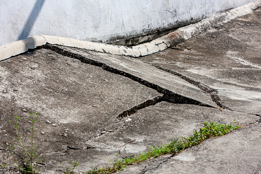 Cracked and damaged, broken concrete road adjoining buildings, due to ground subsidence. Southeast Asia.
