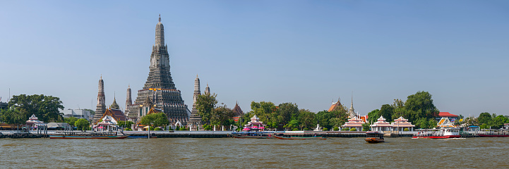 Riverbank panoramic view, looking from the Chao Praya River, of the world-famous riverside temple of Wat Arun, in Bangkok. Wat Arun has a spectacular high decorative stupa set in the heart of the temple complex as well as being in the heart of the city.