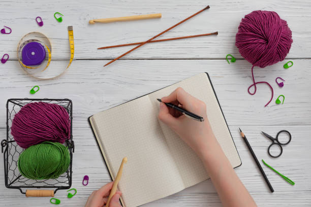 istock Background with knitting and crocheting tools and accessories for starting a project, woman hands writing 1212483624