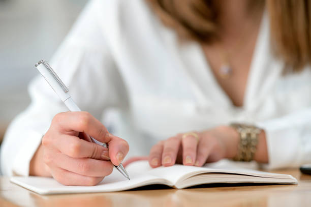istock Close up view of woman hand using pen writing on notebook while sitting at wooden table. Copy space. 1212486998