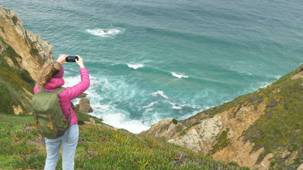 istock woman with large backpack takes picture from ocean coast 1212488900