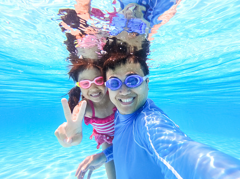 asian cute daughter and father play and selfie happily in the swimming pool
