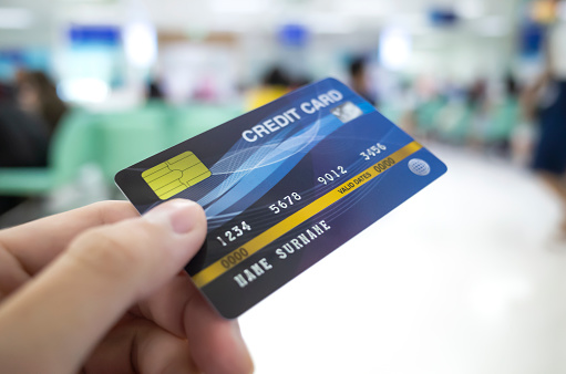 patient hand holding credit card for payment at hospital, blur background of sick people waiting, medical finance concept