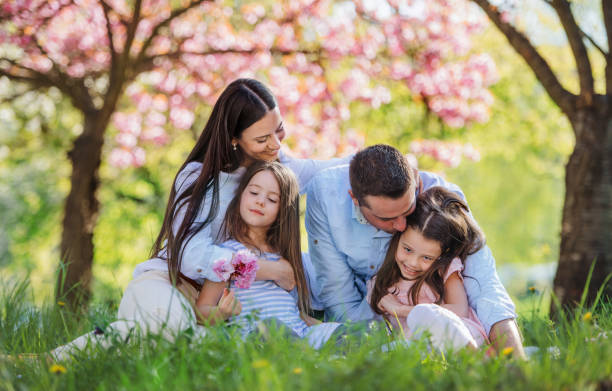 Young parents with small daugthers sitting outside in spring nature.
