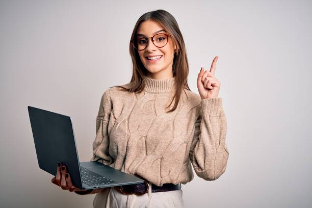 istock Young beautiful brunette woman working using laptop over isolated white background surprised with an idea or question pointing finger with happy face, number one 1212509056