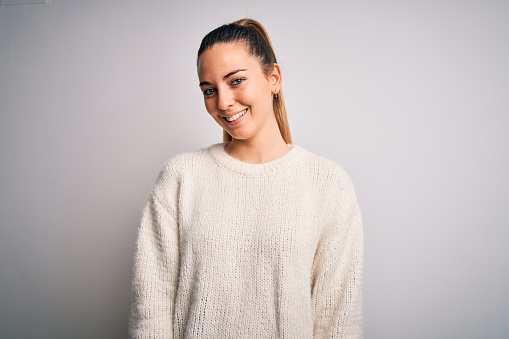 Young beautiful blonde woman with blue eyes wearing casual sweater over white background with a happy and cool smile on face. Lucky person.