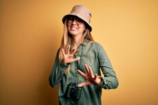istock Beautiful blonde explorer woman with blue eyes wearing hat and glasses using binoculars disgusted expression, displeased and fearful doing disgust face because aversion reaction. With hands raised 1212512821